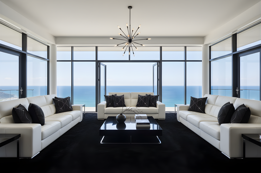 Modern living room with white sofas, black coffee table, and large windows overlooking the ocean.
