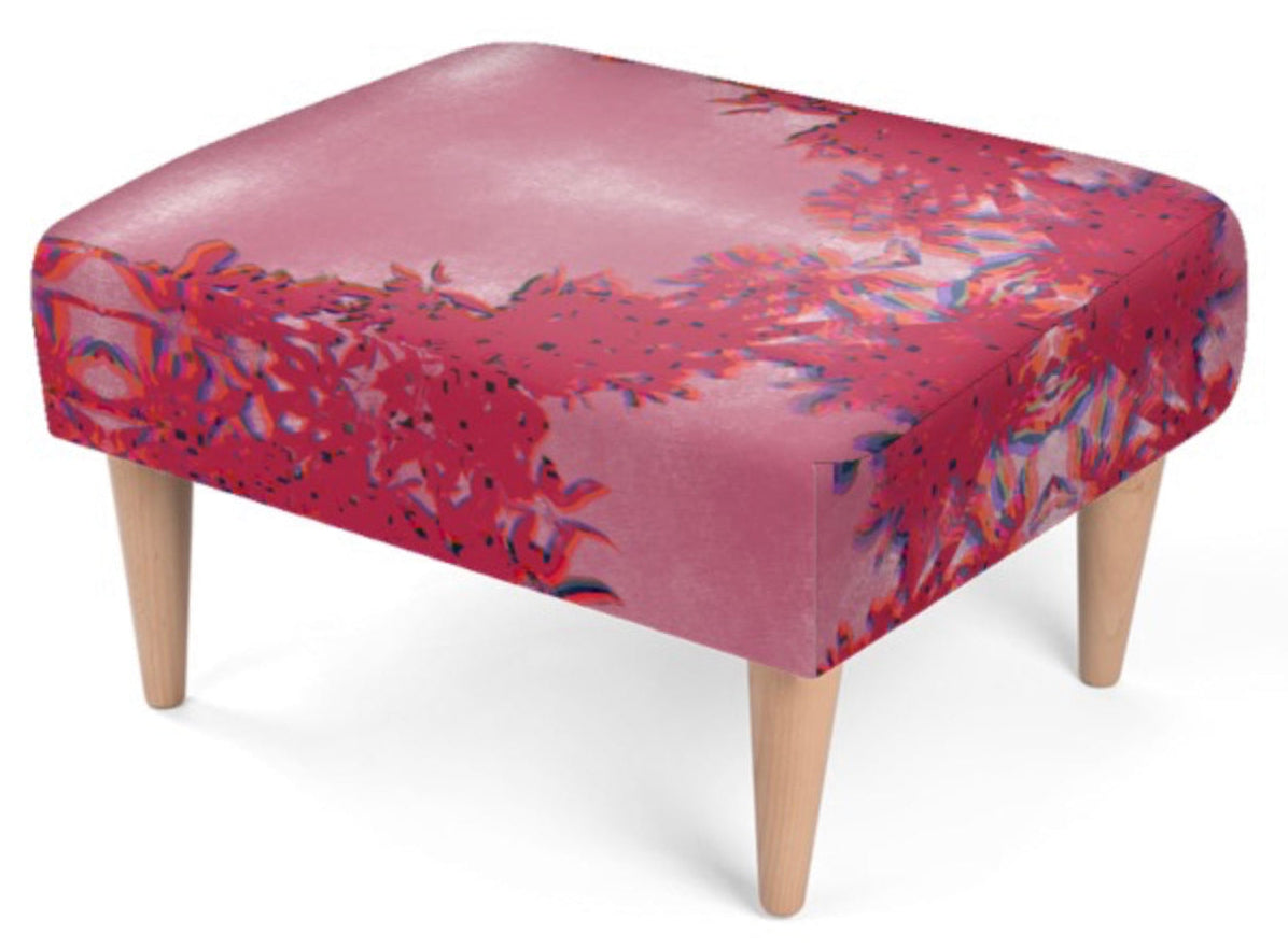 A square upholstered foot rest with a pink and red botanical patterned fabric and four tapered light wood legs, shown on a white background.