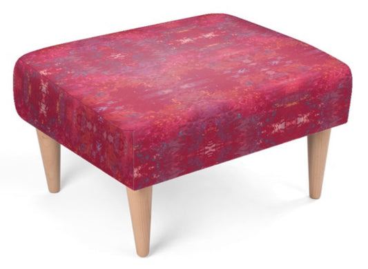 A square upholstered footstool with a distressed red and purple patterned fabric top and four tapered light wood legs, shown on a plain white background.