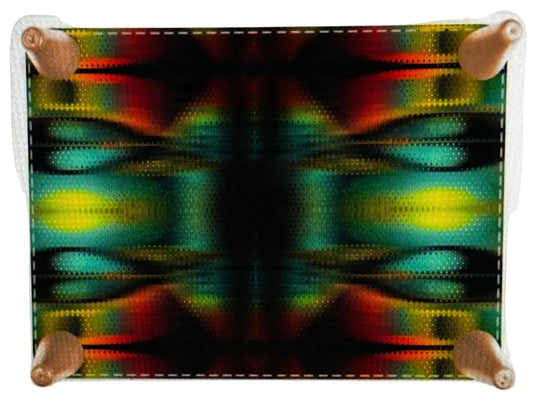 A square fabric art print or patch with a colorful abstract symmetrical pattern, secured with four wooden pegs on a white textured background.