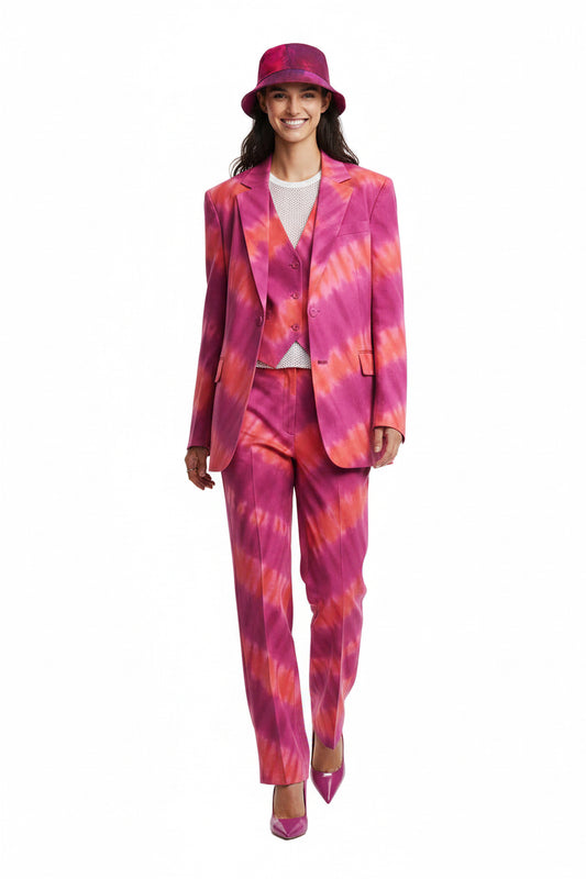 A woman modeling a vibrant pink and orange tie-dye suit set, including a blazer, matching trousers, a matching hat, and pointed shoes, against a plain white background.