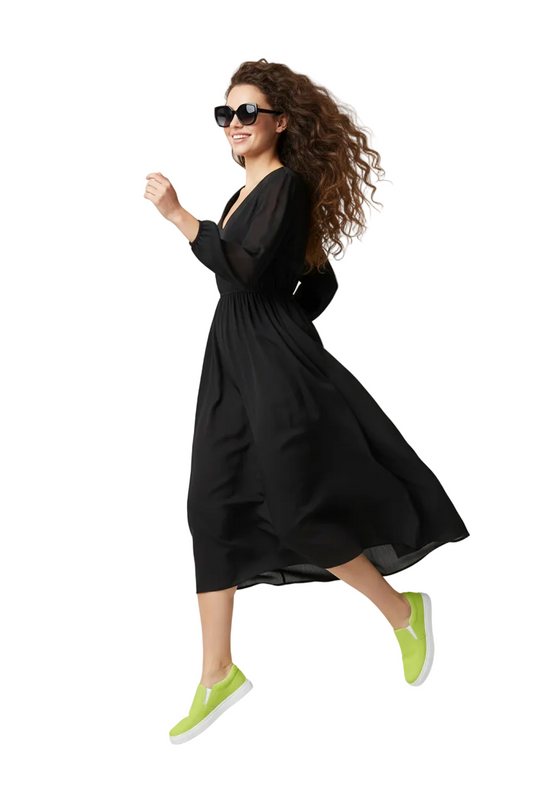 Woman wearing a black dress with a flowing skirt, KhuKhuZ neon green shoes, and sunglasses on a white background