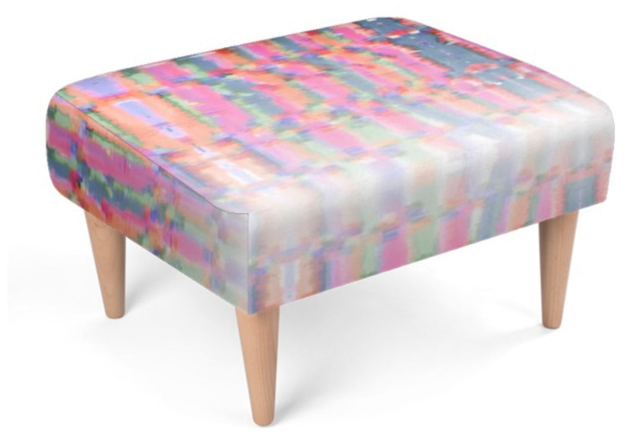A square upholstered footstool with a colorful abstract watercolor pattern in pink, blue, purple, and green, supported by four tapered light wood legs on a white background.