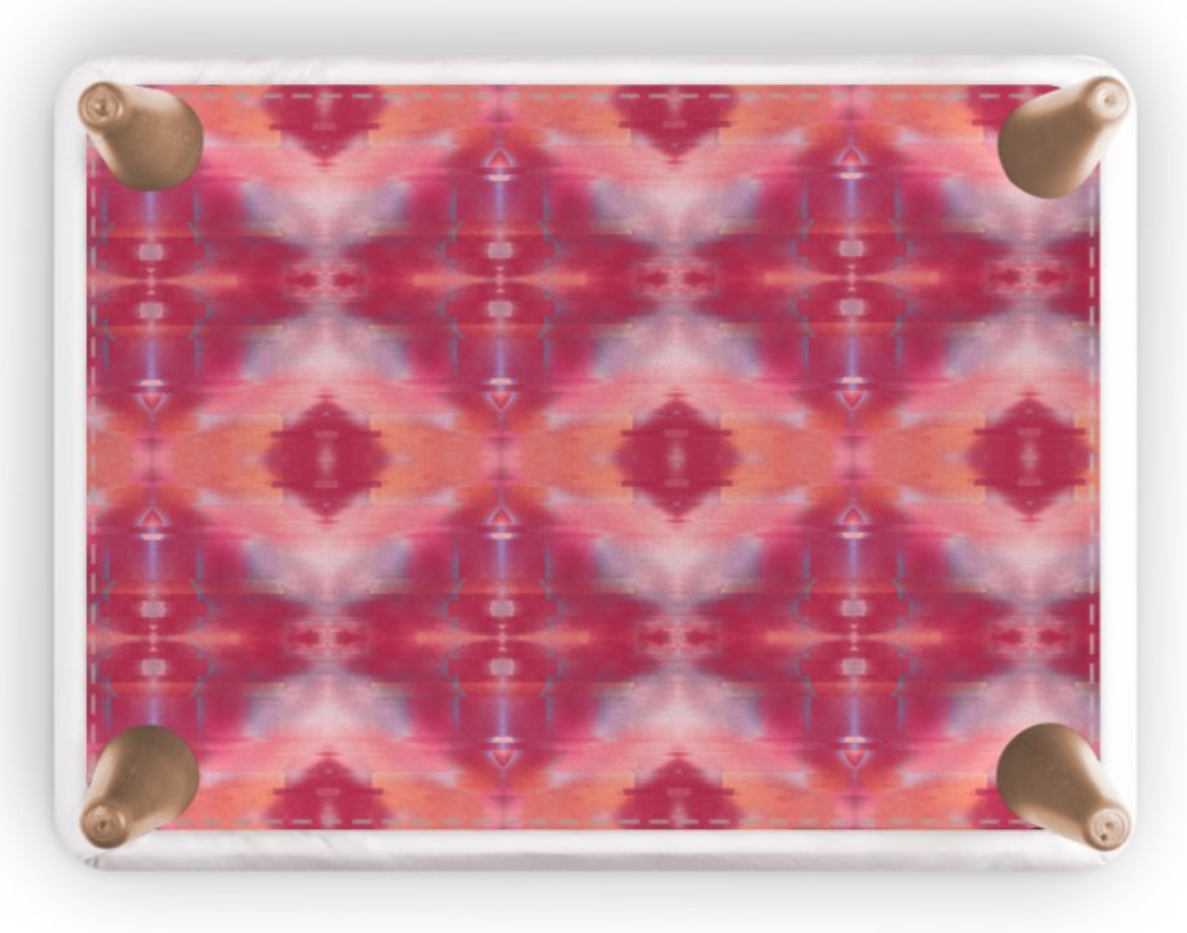 A rectangular footstool with rounded corners and four metallic rose gold feet, featuring a vibrant pink, red, and orange kaleidoscopic pattern on a white background.