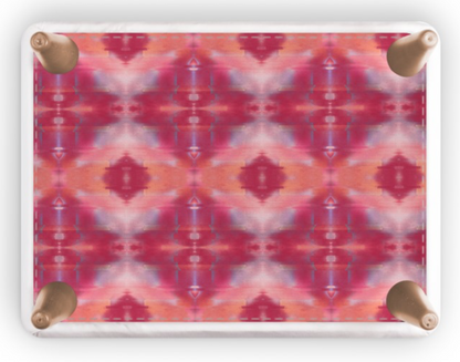 A rectangular footstool with rounded corners and four metallic rose gold feet, featuring a vibrant pink, red, and orange kaleidoscopic pattern on a white background.