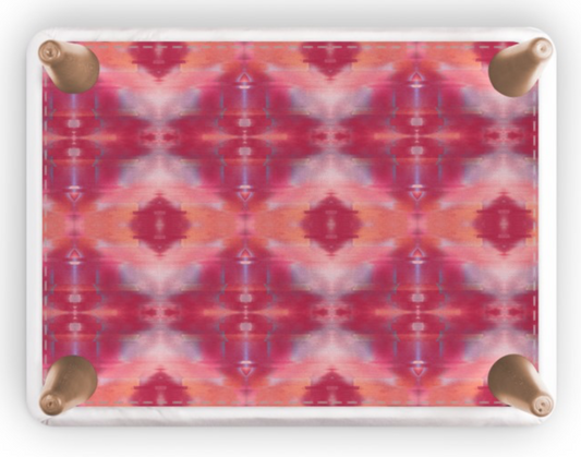 A rectangular footstool with rounded corners and four metallic rose gold feet, featuring a vibrant pink, red, and orange kaleidoscopic pattern on a white background.