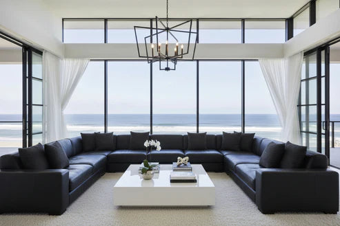 Modern living room with black sectional sofa, white coffee table, and large windows overlooking an ocean view, with BP Interiors monochrome cushions small circles print design