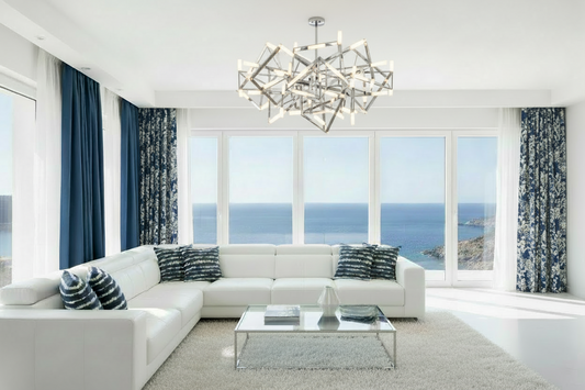 Modern living room with a white sectional sofa, blue striped pillows, and large windows overlooking the ocean.