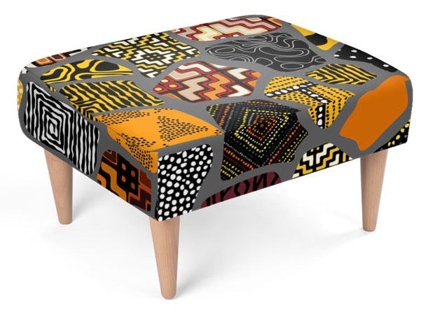 A square upholstered footstool with a bold geometric and tribal-inspired pattern in orange, yellow, black, white, and gray, supported by four light wood legs on a white background.