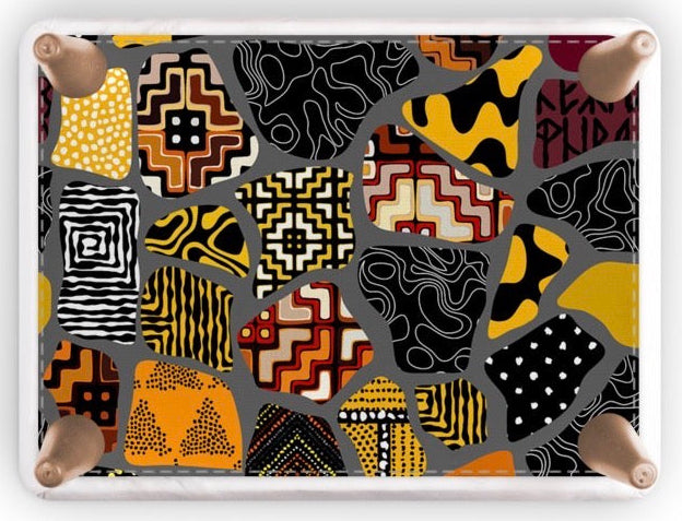A footstool with a colorful abstract patchwork pattern featuring black, yellow, orange, red, and white geometric and organic motifs, framed by a white border with four natural wood legs on a white background.