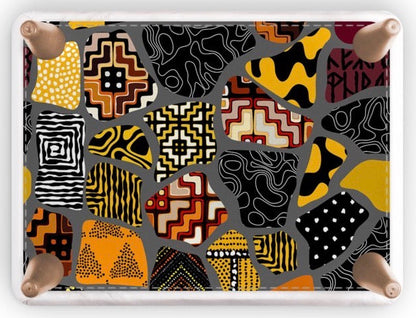 A footstool with a colorful abstract patchwork pattern featuring black, yellow, orange, red, and white geometric and organic motifs, framed by a white border with four natural wood legs on a white background.