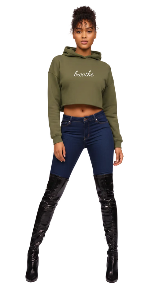 Woman wearing a green cropped hoodie with 'breathe' text, blue jeans, and black knee-high boots on a white background.