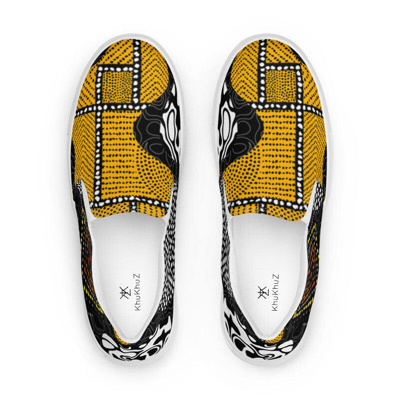 A pair of slip-on canvas shoes shown from a top-down view, featuring a bold yellow, black, and white geometric pattern inspired by African wax print, with the brand name 'Khaitinuz' printed on the white insoles.