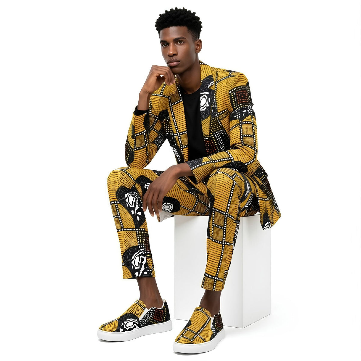 A pair of slip-on canvas sneakers featuring a vibrant yellow and black African wax print pattern, white soles, and white interior lining, shown against a plain white background.