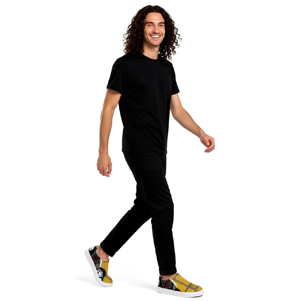 A pair of slip-on canvas sneakers featuring a vibrant yellow, black, and white African wax print pattern, with white rubber soles, shown on a clean white background.
