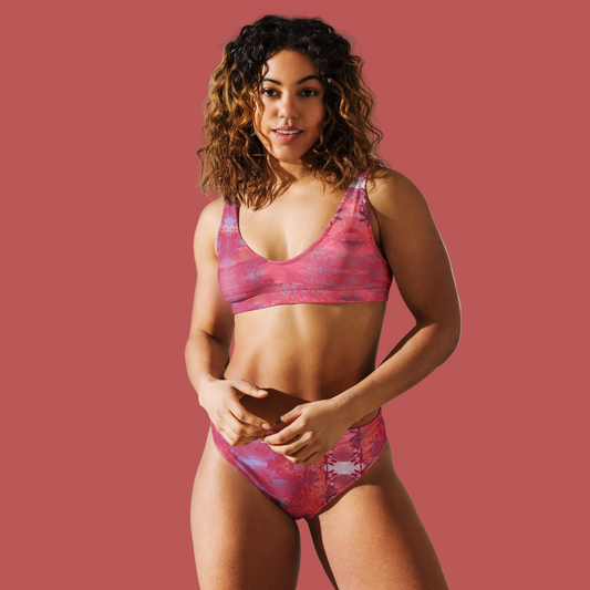 Woman wearing a pink patterned bikini standing against a neutral wall.