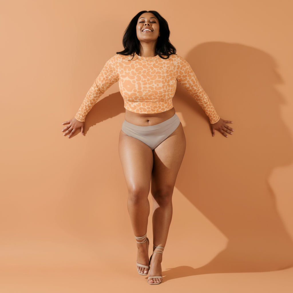 Woman wearing an orange patterned long-sleeve crop top and beige shorts against a neutral background