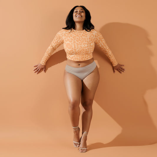 Woman wearing an orange patterned long-sleeve crop top and beige shorts against a neutral background