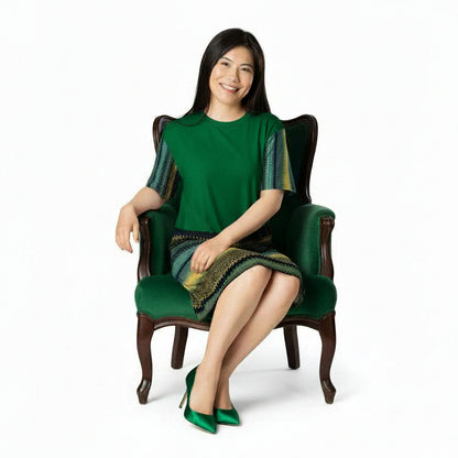 Woman wearing a green dress with patterned sleeves sitting n an elegant green chair