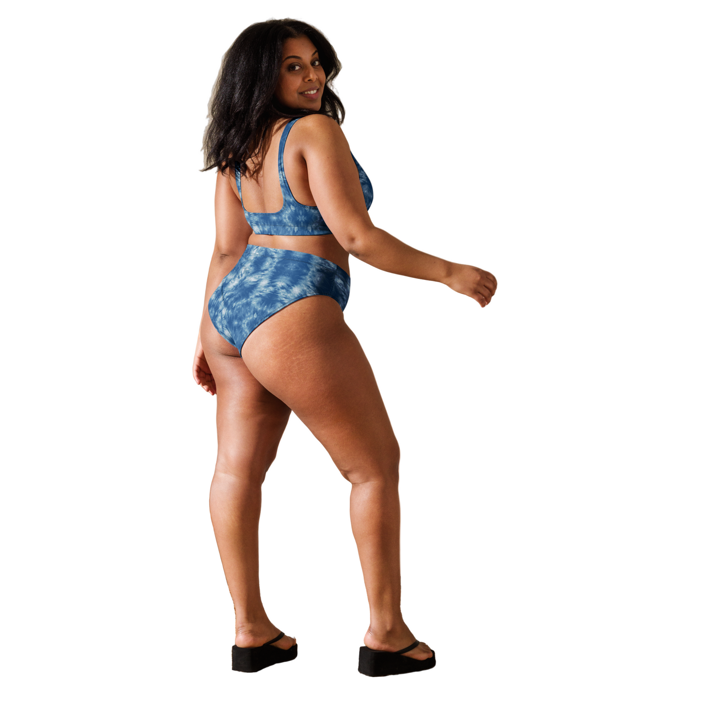 Woman wearing a blue tie-dye bikini standing in a sunlit room with a woven chair and basket.