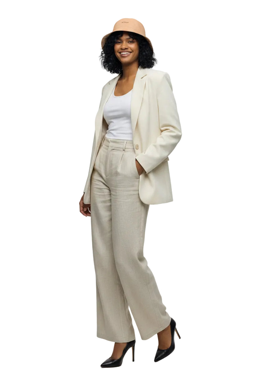 Woman wearing a white sleeveless top and high-waisted white pants with a beige hat on a white background