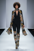 Model walking on a runway wearing a patterned outfit with a black top and pants.