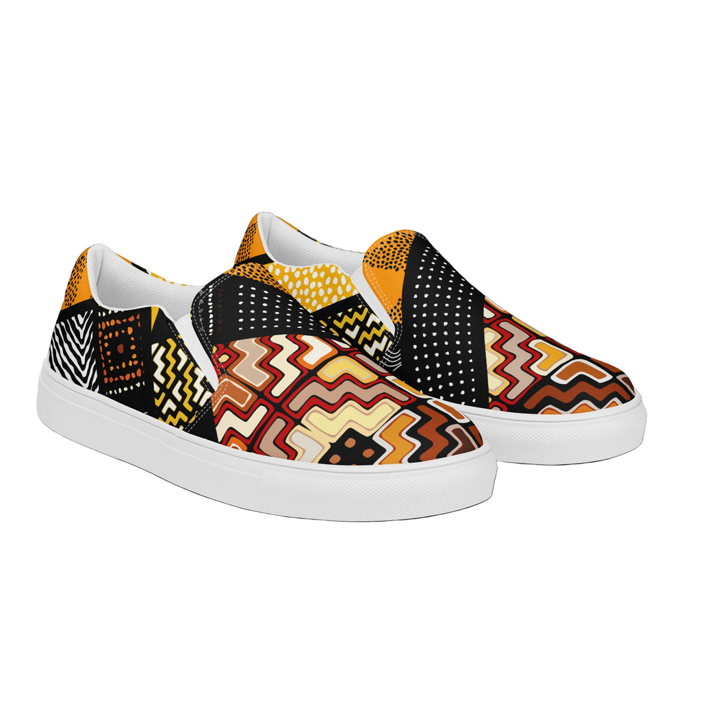 A pair of slip-on canvas sneakers with a vibrant, multicolor geometric and tribal-inspired pattern featuring zigzags, dots, and stripes in black, yellow, orange, red, and white, set against a plain white background.
